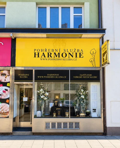 Provozovna Pohřební služby Harmonie na ulici Lidická 44 v Brně se žlutým vývěsním štítem a výlohou s urnami, lucernami a květinovými aranžmá.