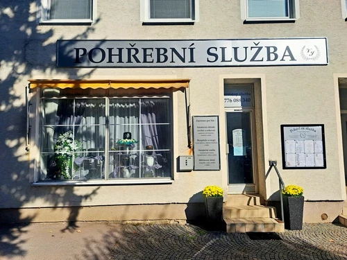 Provozovna pohřební služby s logem Viktor Jungkind – Kukleny, výloha s urnami a smutečními kyticemi, tabule s nabídkou služeb a žluté chryzantémy u vchodu