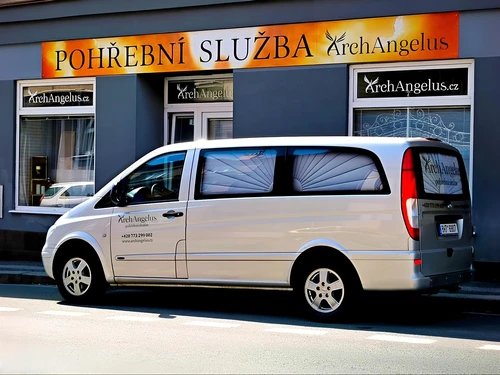 Provozovna pohřební služby ArchAngelus s prosklenou výlohou a stříbrný pohřební vůz zaparkovaný před vchodem.