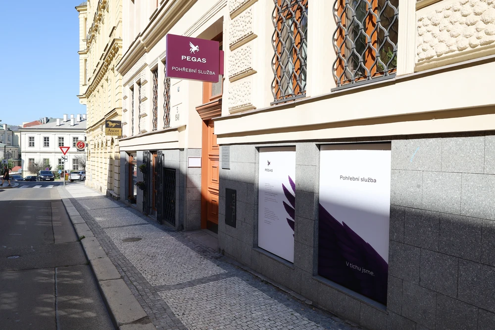 Provozovna Pohřební služby Pegas v historickém domě s vínovým vývěsním štítem s logem pegasa a polepenými okny s nápisem pohřební služba.