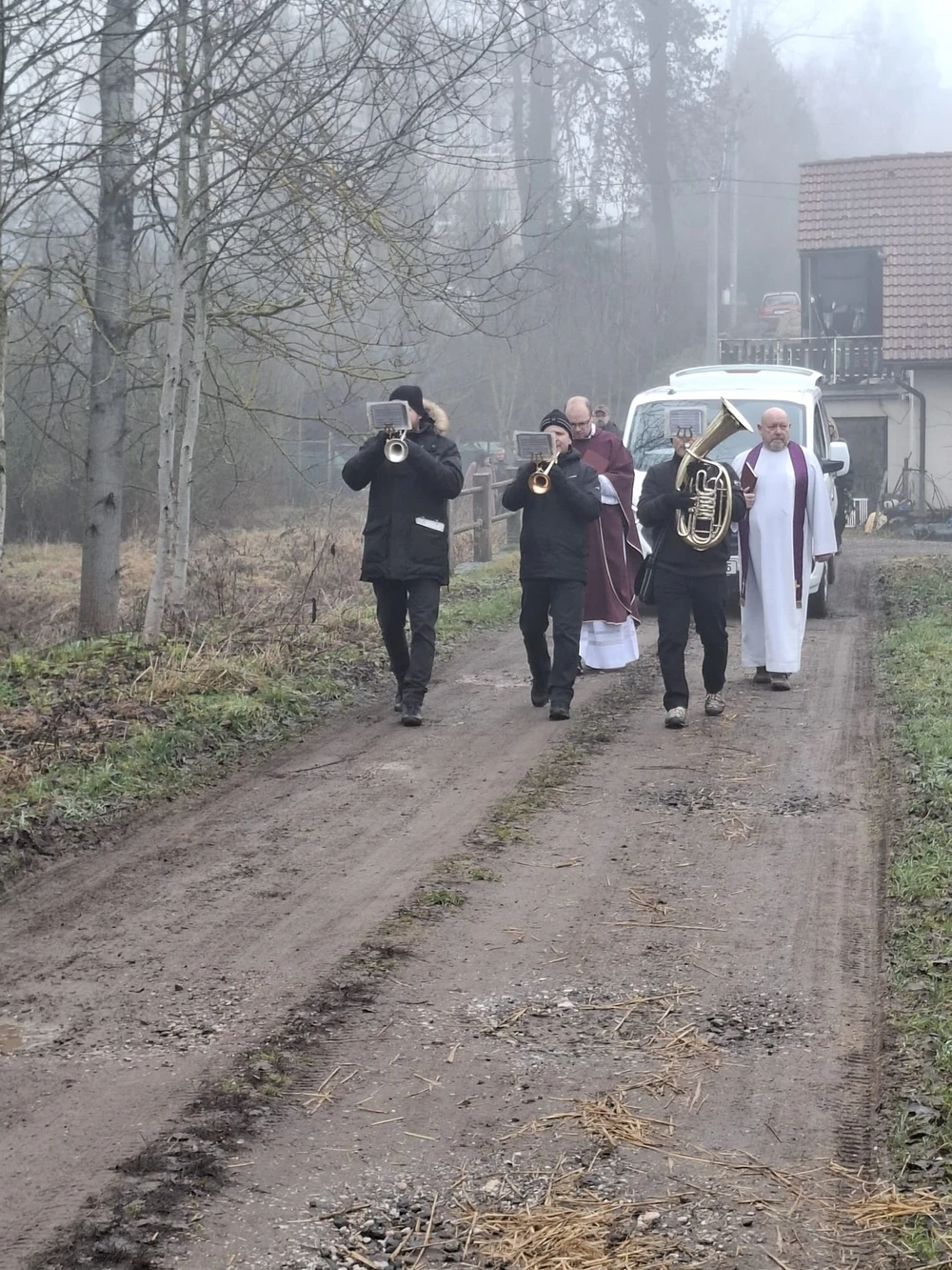 Pohřební průvod s dechovou hudbou a knězem v mlhavé krajině, pohřební vůz Bělohoubek na polní cestě